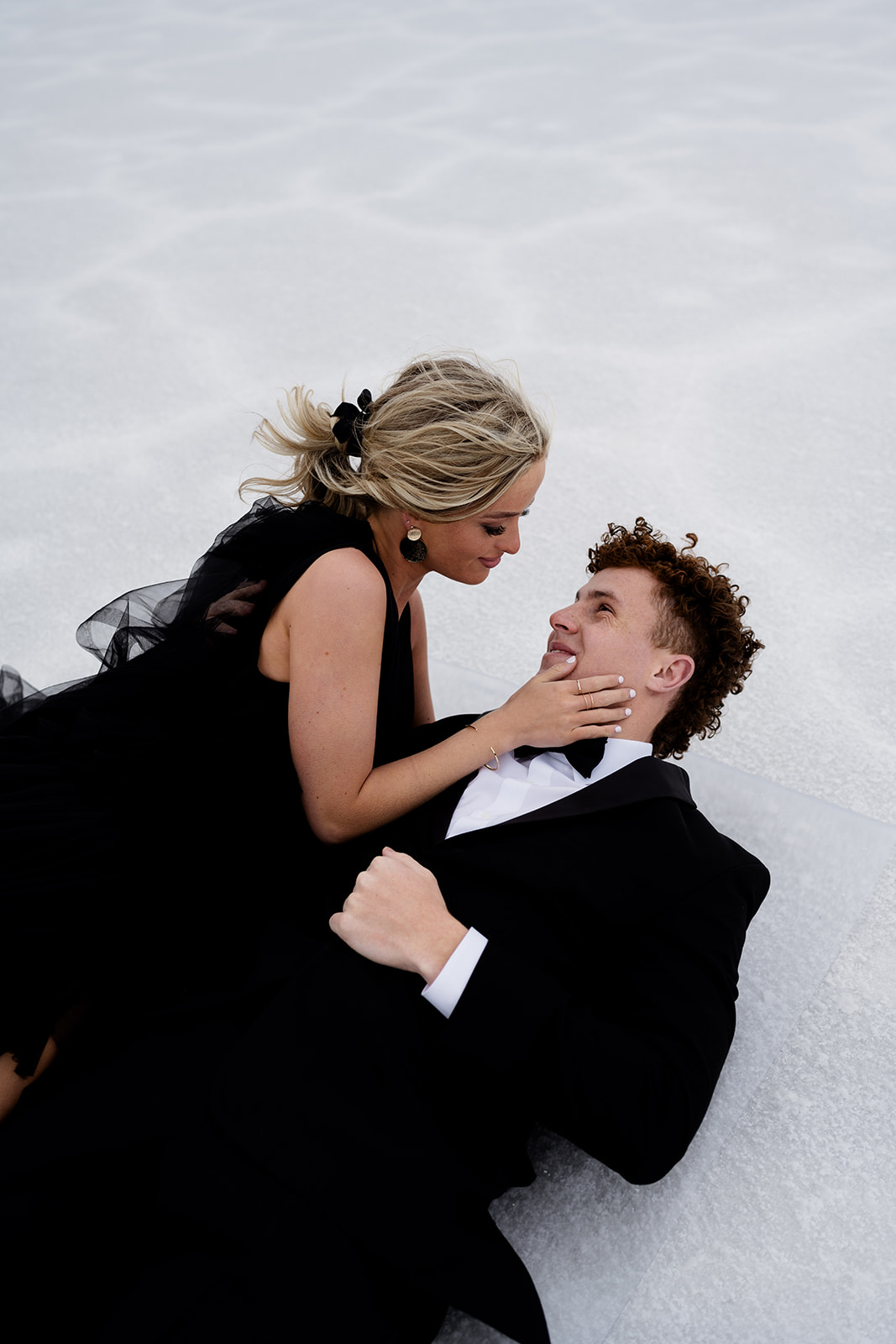 Couple gazes lovingly in each other eyes while laying on the salt at Utah Salt Flats