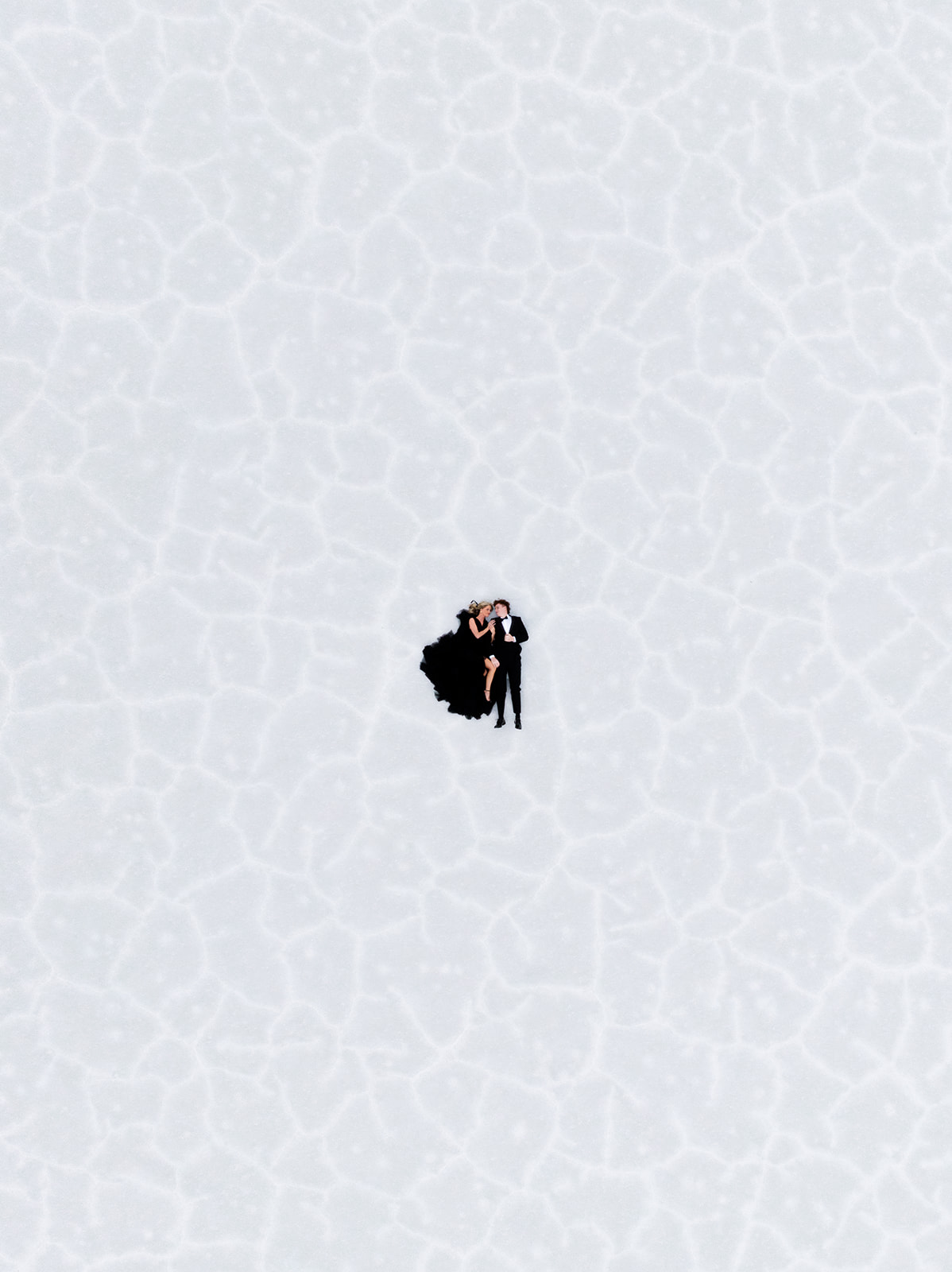 drone birds eye view of a couple in black formal wear laying on the salt flats in utah