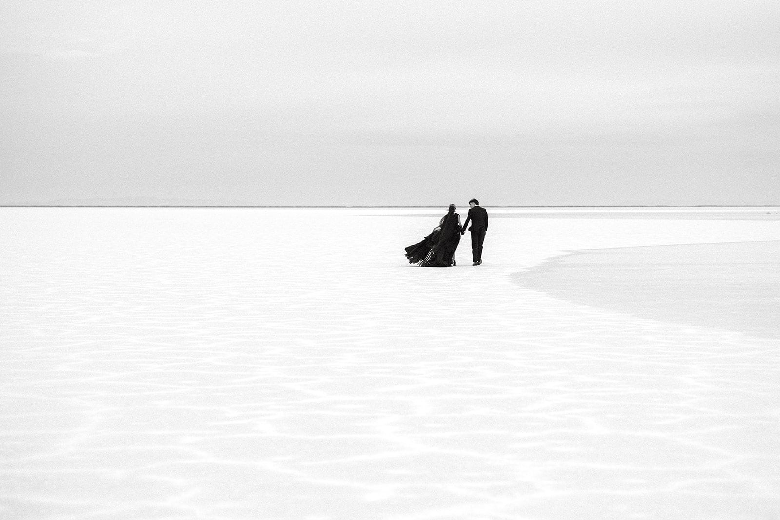 Sweeping views of wedding couple walking the Utah Salt Flats during couple’s elopement photoshoot