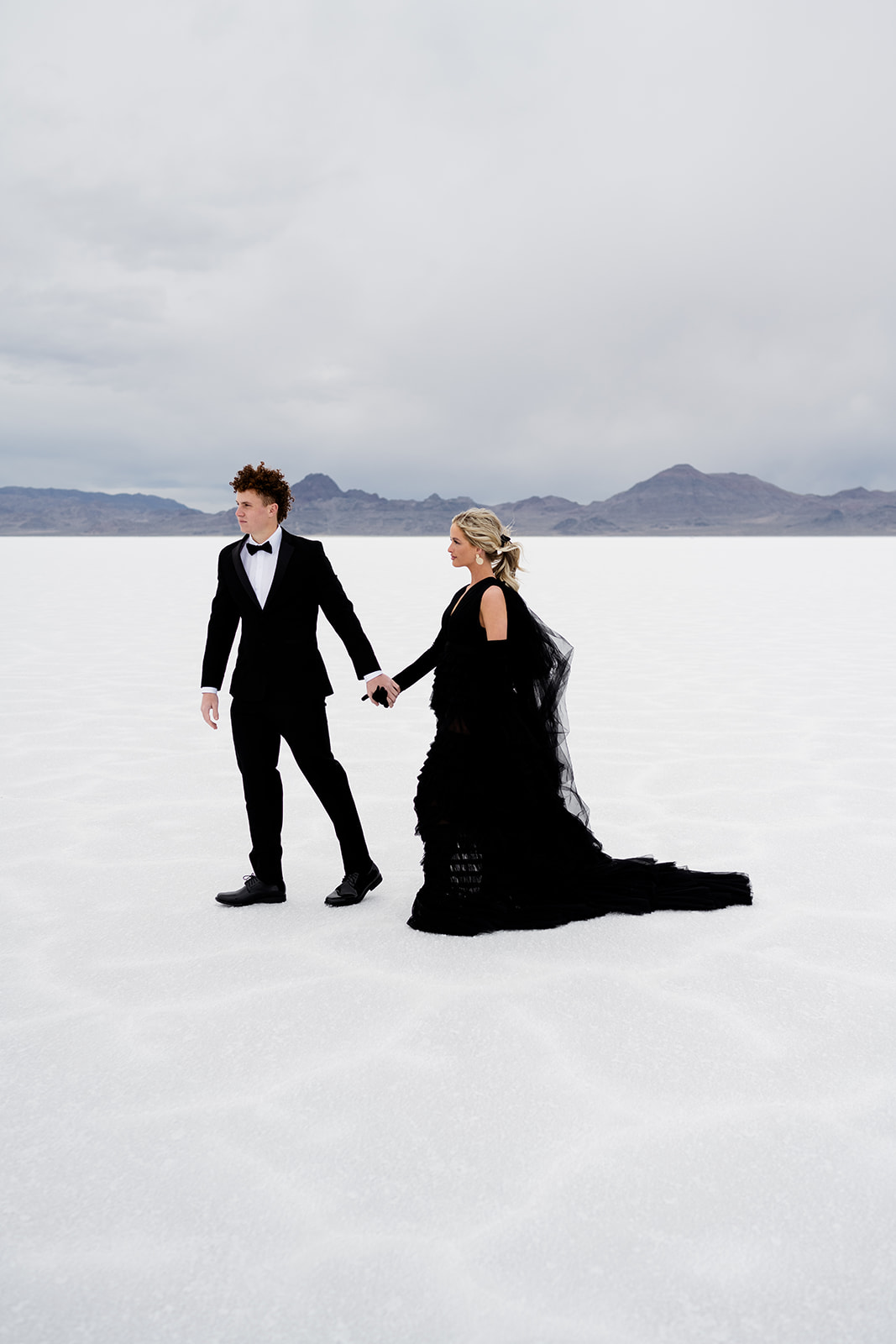 Utah Salt Flats’ timeless landscape embraces couple in black wedding attire.