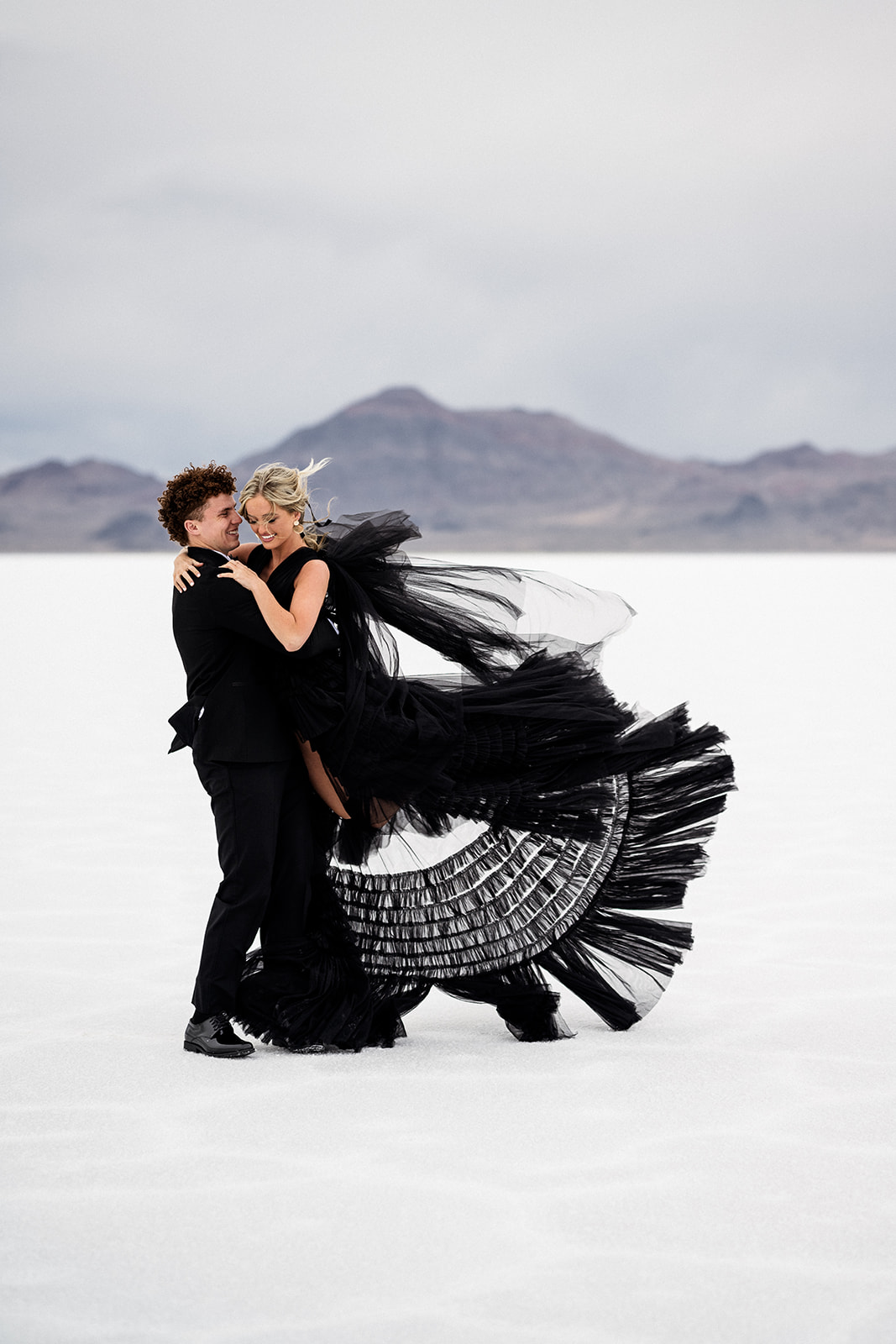 Utah Salt Flats wedding shoot capturing couple’s playful spin in a black tux and black dress
