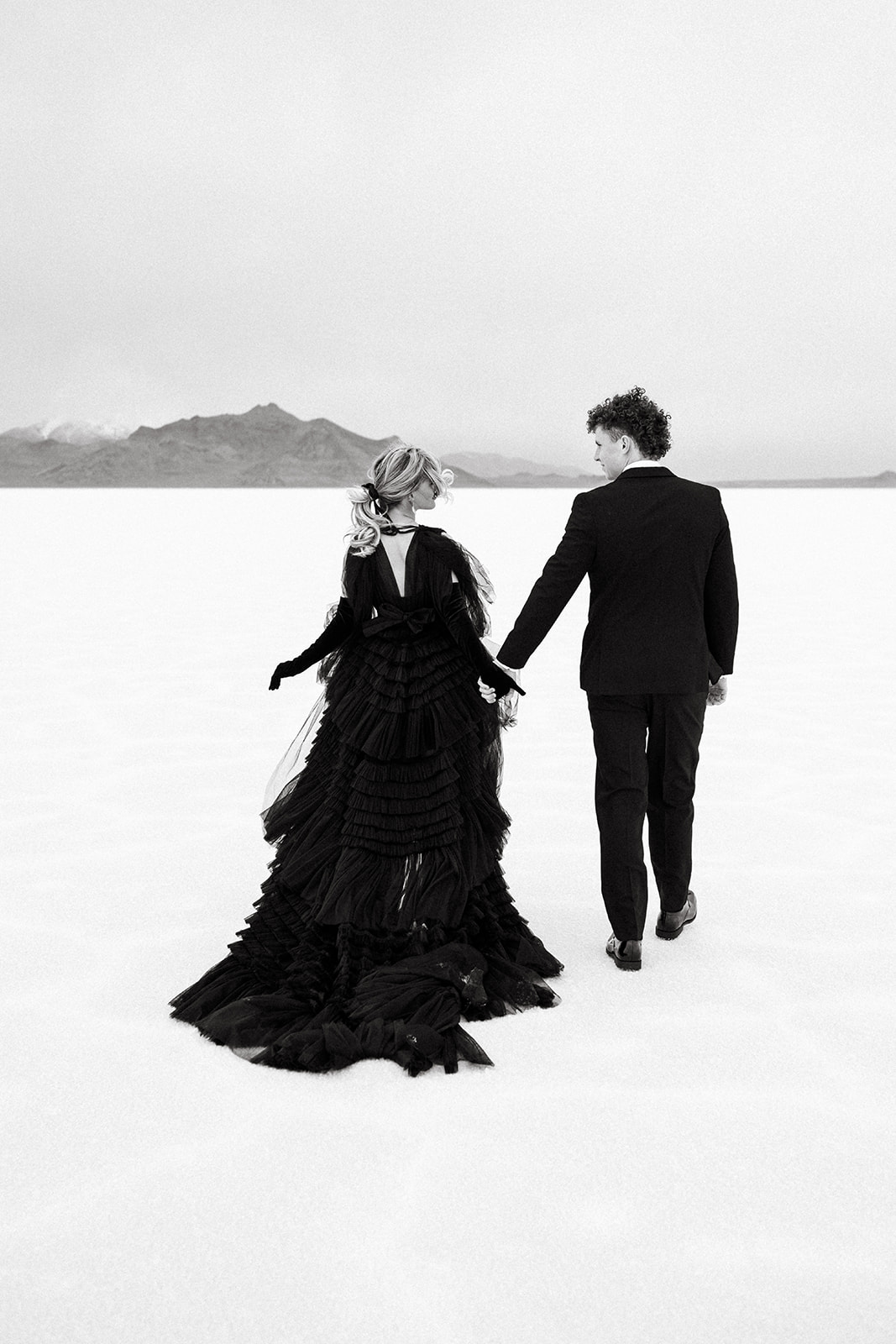 Utah wedding photographer captures couple holding hands and walking in the mountains at Bonneville Salt Flats