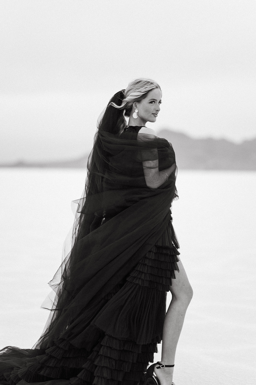women in a black dress and black tulle standing looking off into the distance at the salt flats