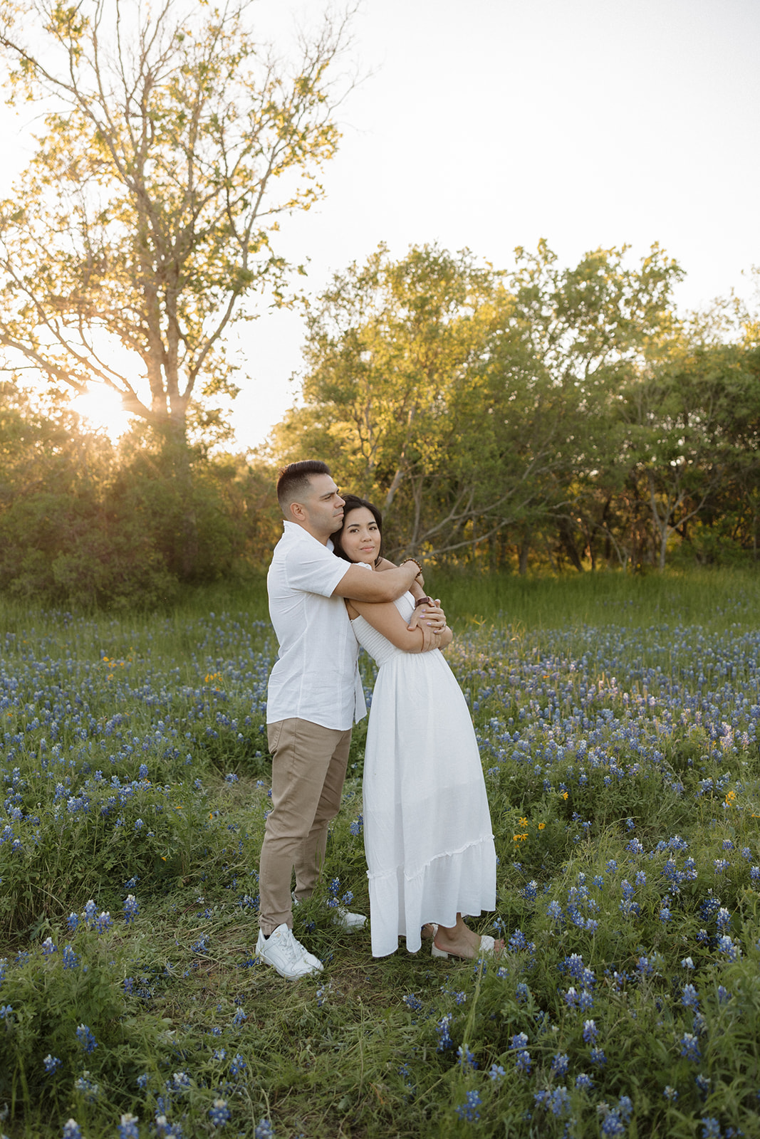Couple wearing white hugging in a field of Bluebonnets h at McKinney Falls state park