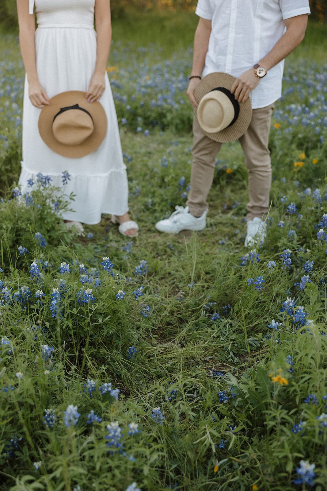 Couple standing in field of Bluebonnets holding hats at McKinney Falls state park